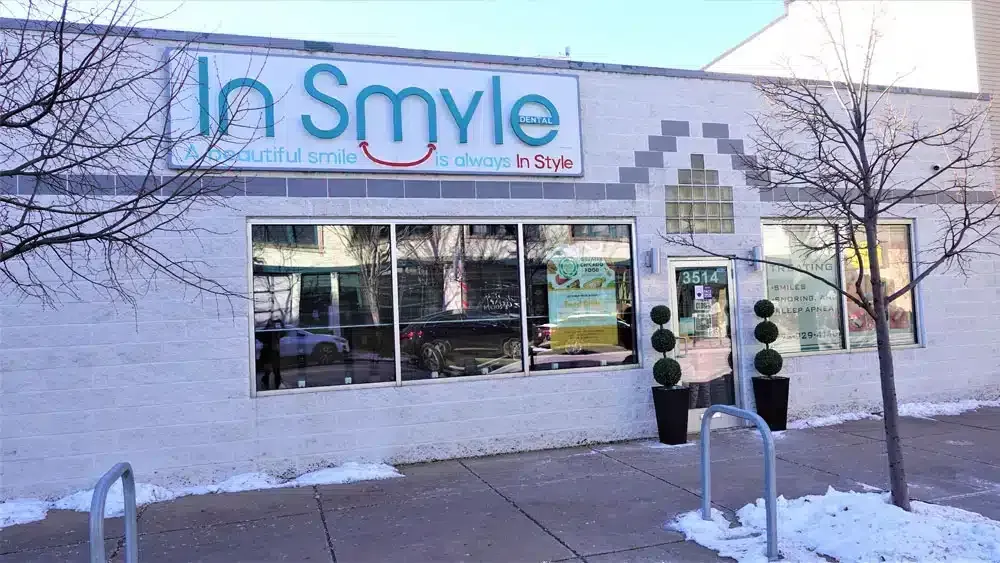 Storefront of "In Smyle Dental" with large sign, windows, topiary plants, and snow patches.