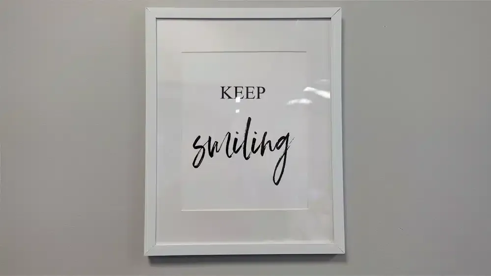 White framed print reading "Keep Smiling" hanging on a gray wall.