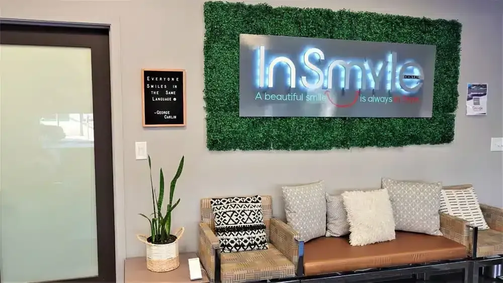 Dental office waiting area with "InSmyle" sign on green wall, sofa, and plant.