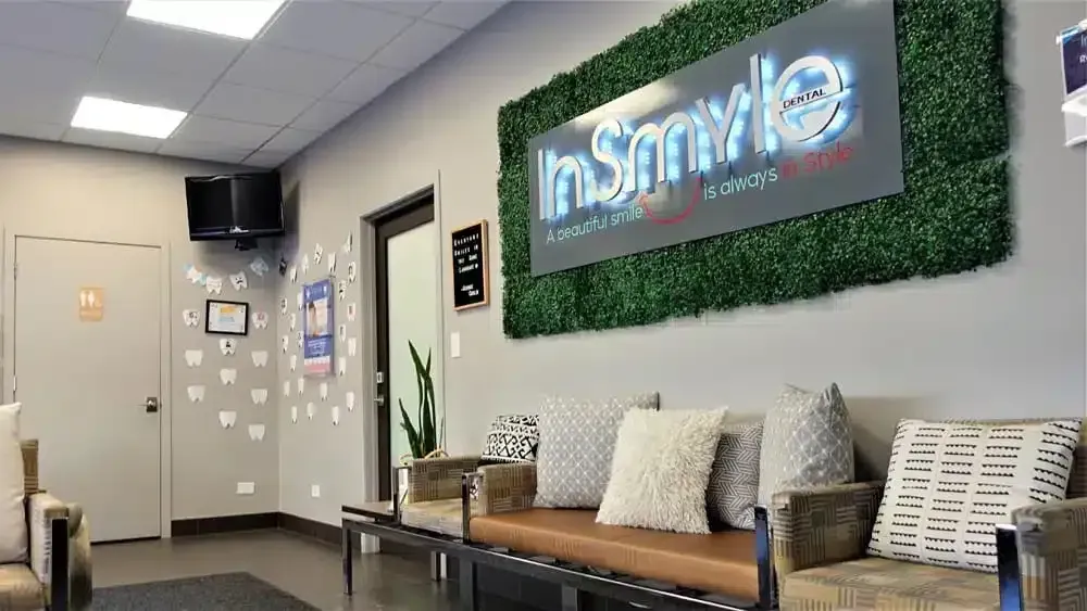 Dental office waiting room with "InSmyle Dental" sign on artificial green wall above seating.